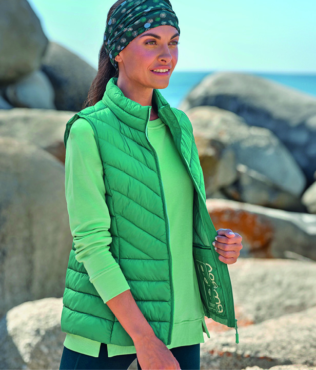 A woman in green Roama activewear, stretching outdoors.